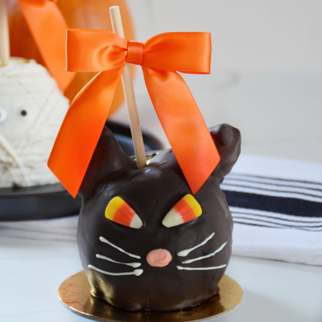 Halloween caramel apple dipped in dark chocolate and shaped like a cat with evil candy corn eyes